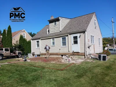 A construction worker prepares the backyard site for a new deck installation after removing the previous structure, leaving debris and marked boundaries.