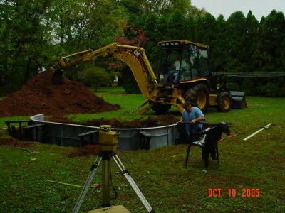 Workers use heavy machinery and tools to excavate and install the structural framework for an in-ground swimming pool in a residential backyard.